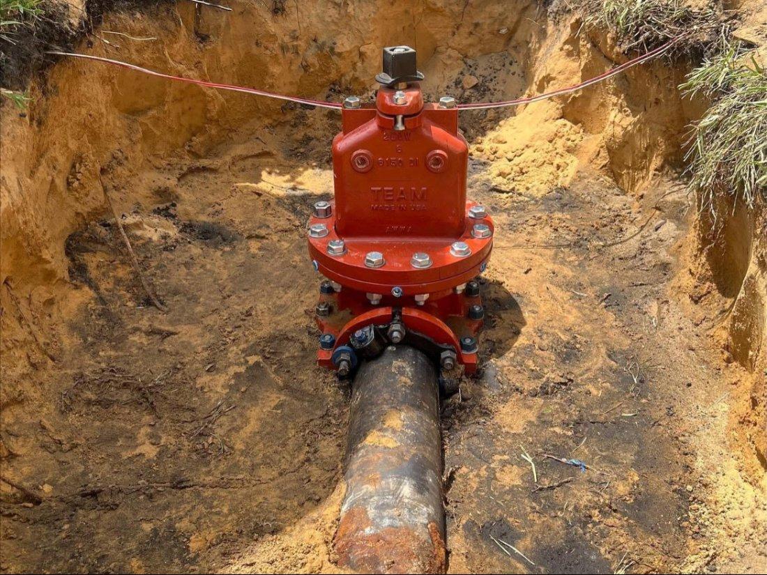 Red pipeline insertion valve installed on an underground water main with exposed soil and utility markings.