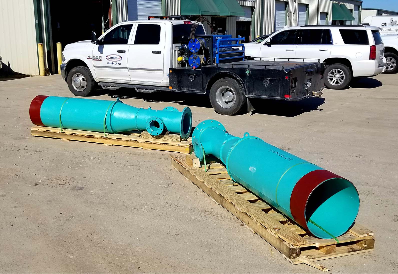 Two large pipes placed over wooden pallets on a concrete floor with some dirt next to a towing truck outdoors.